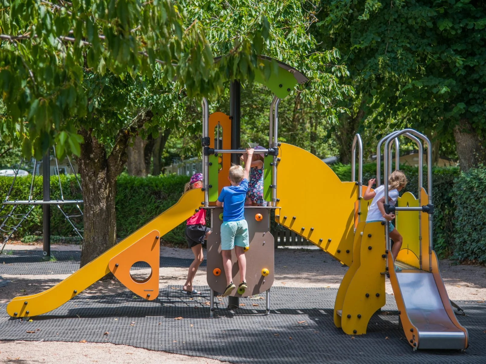Enfants qui grimpent et glissent sur l'aire de jeux ombragée du camping