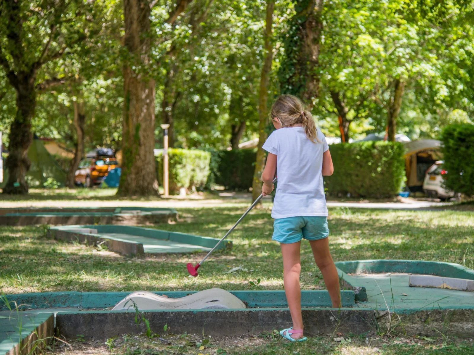 Enfant qui joue au mini-golf sous les arbres au camping Saint Lambert