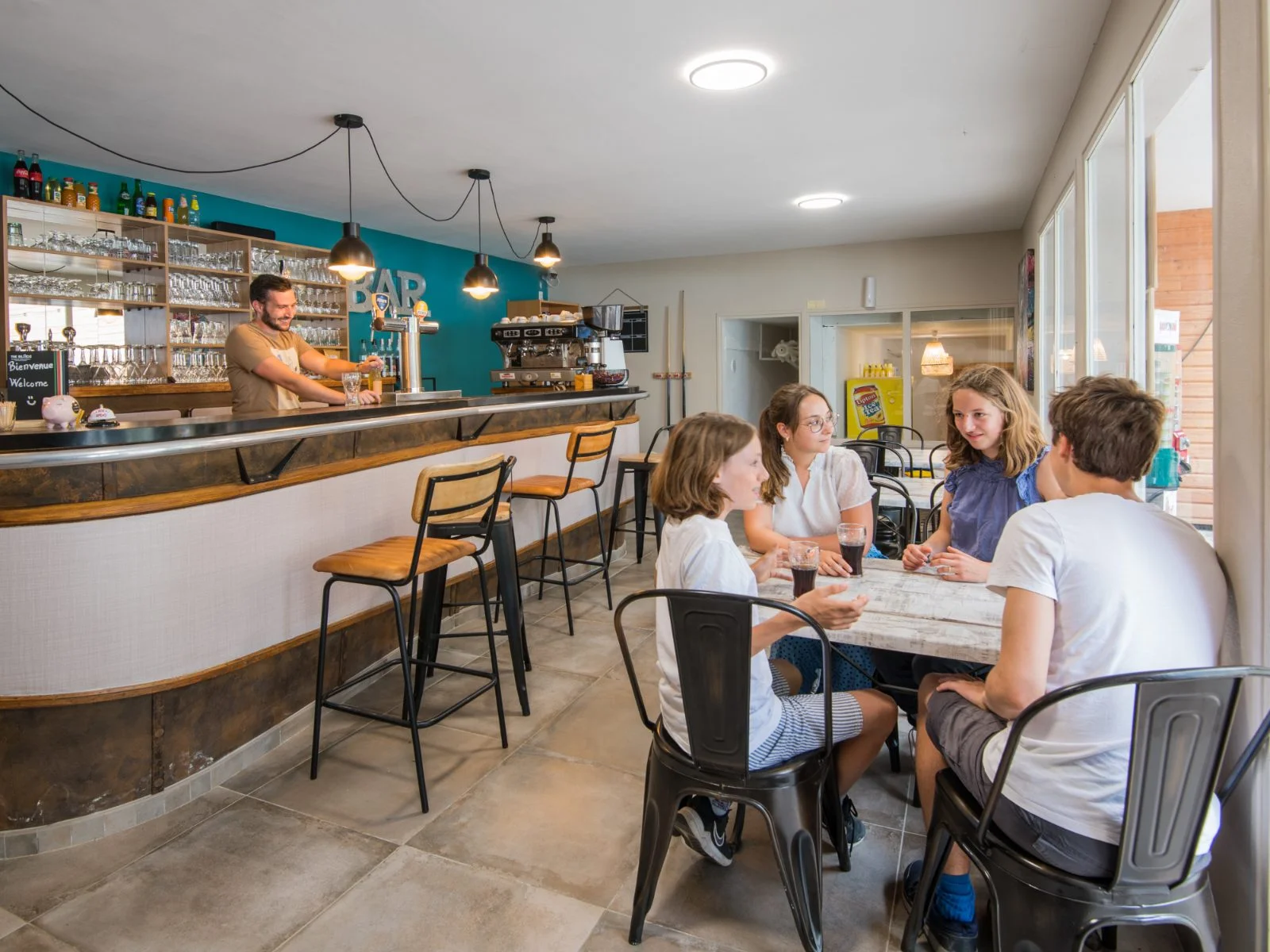 Bar intérieur du camping avec barman au comptoir et clients attablés