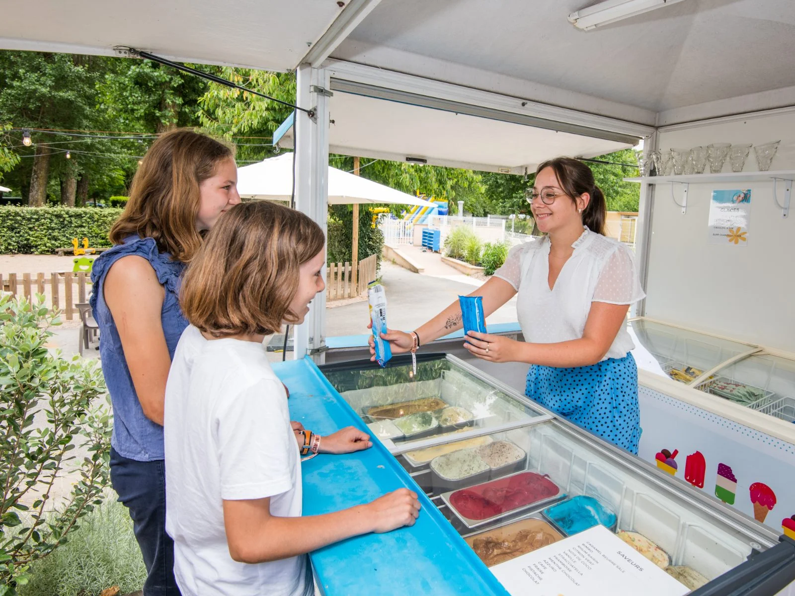 Comptoir glaces du camping avec vendeuse servant deux jeunes clientes