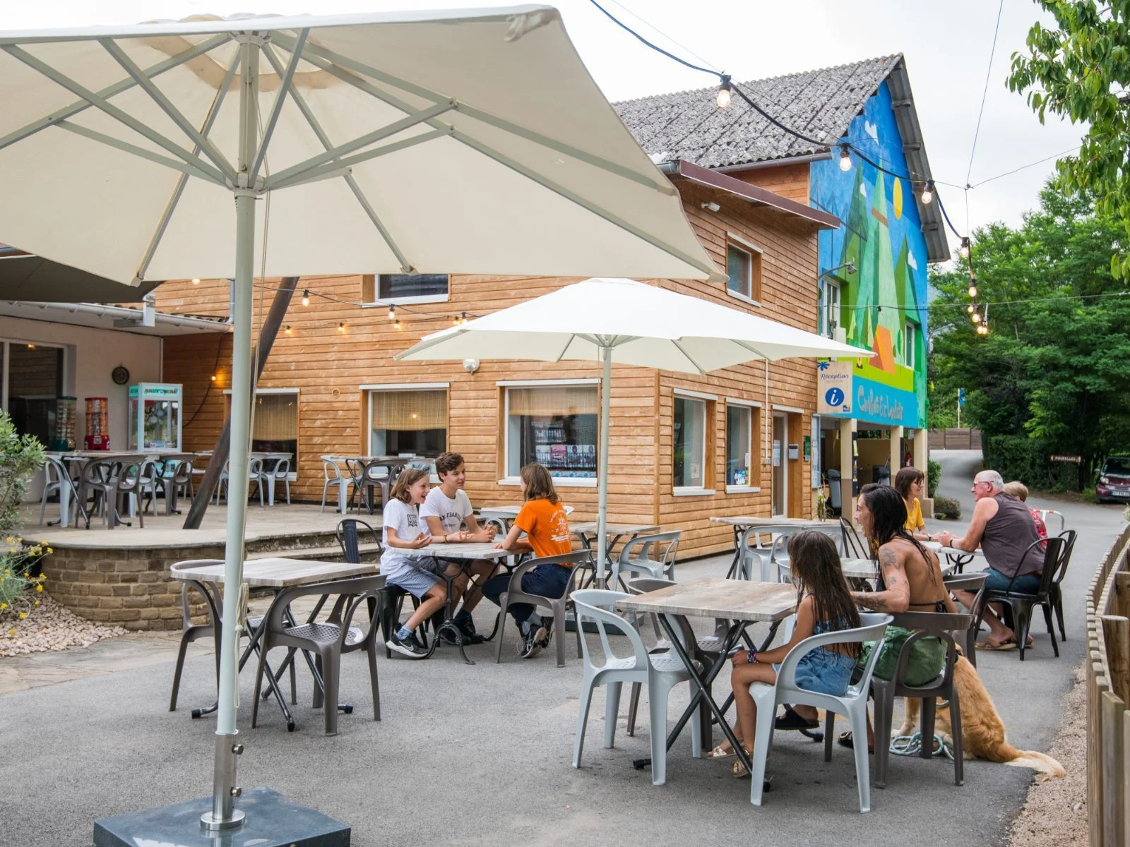 Terrasse du snack-bar du camping avec familles attablées sous les parasols